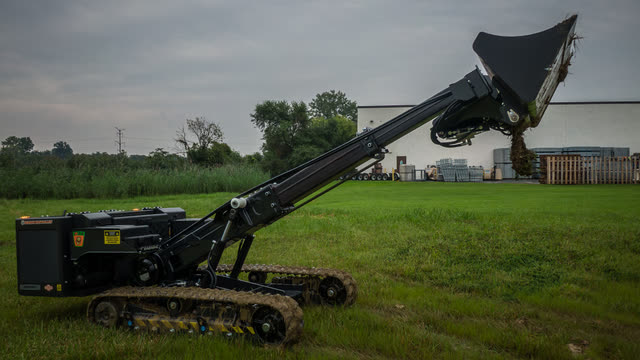 Tracked loader tipping a bucket at the top of its boom.